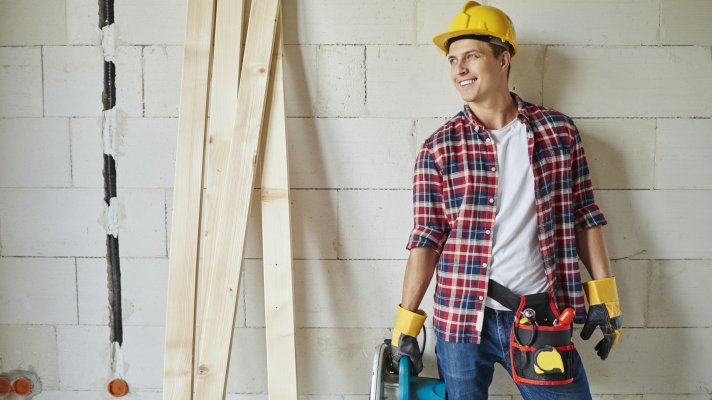 Young carpenter is holding electric saw and looking away